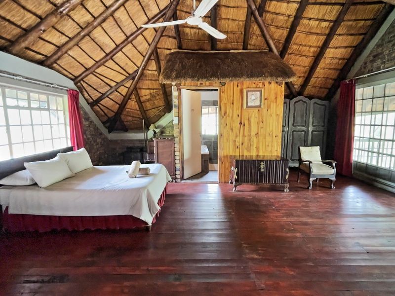 Spacious bedroom featuring a high thatched roof with exposed rafters, timber flooring, and direct access to an outdoor area through sliding glass doors.