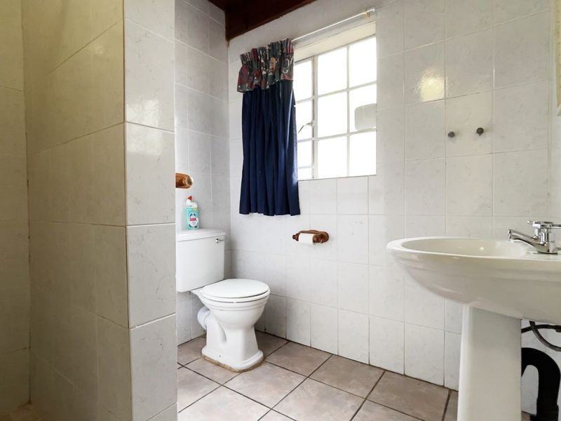 A functional bathroom featuring a pedestal basin, toilet, and tiled shower enclosure with classic white wall tiling.