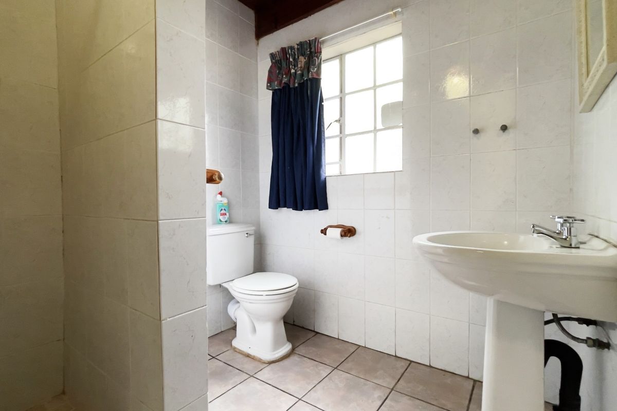 A functional bathroom featuring a pedestal basin, toilet, and tiled shower enclosure with classic white wall tiling.