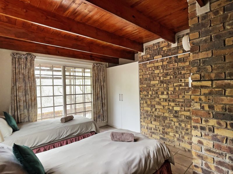 A bedroom featuring exposed timber ceiling beams, a rustic brick feature wall, tiled flooring, and a built-in wardrobe with access to a patio.