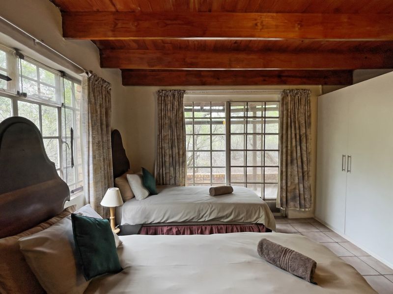 Spacious bedroom featuring exposed timber ceiling beams, an exposed brick feature wall, tiled flooring, and direct access to the outdoors via sliding glass doors.