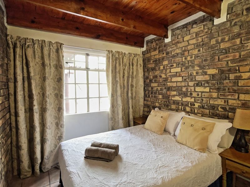 Cozy bedroom featuring rustic exposed brick walls and exposed timber ceiling beams, creating a warm and character-filled living space.