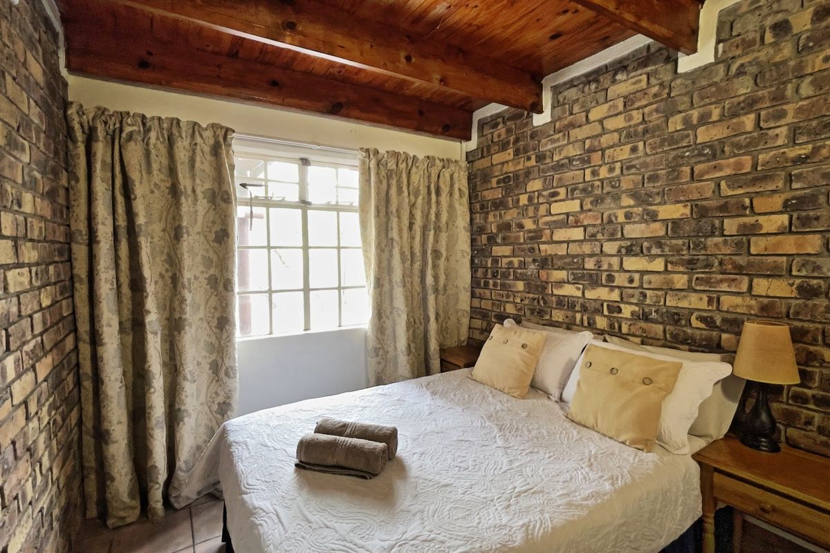 Cozy bedroom featuring rustic exposed brick walls and exposed timber ceiling beams, creating a warm and character-filled living space.