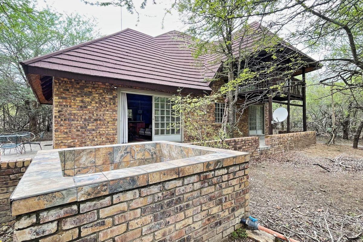 Rear view of a face brick house featuring a raised patio, balcony, and a brick-built water feature set within a natural bushveld environment.