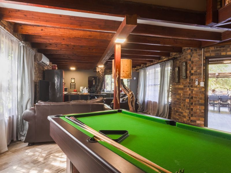 Spacious living area featuring exposed timber ceiling beams, rustic face brick walls, and tiled flooring, with direct access to an outdoor patio.