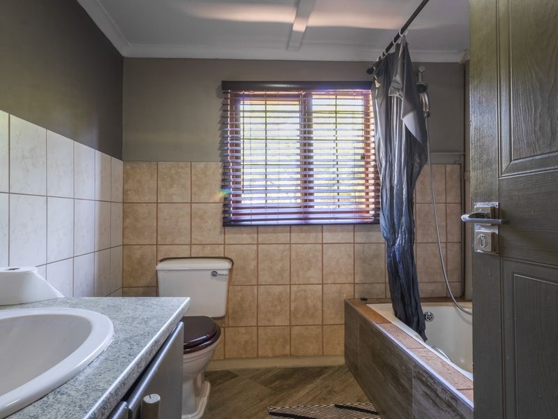 A functional bathroom featuring a vanity basin, toilet, and a bathtub with an integrated shower head, finished with neutral wall tiling.