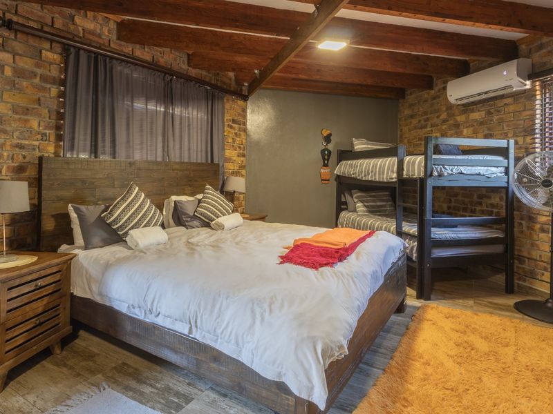 A rustic-style bedroom featuring exposed brick walls, timber ceiling beams, and a split-system air conditioner.