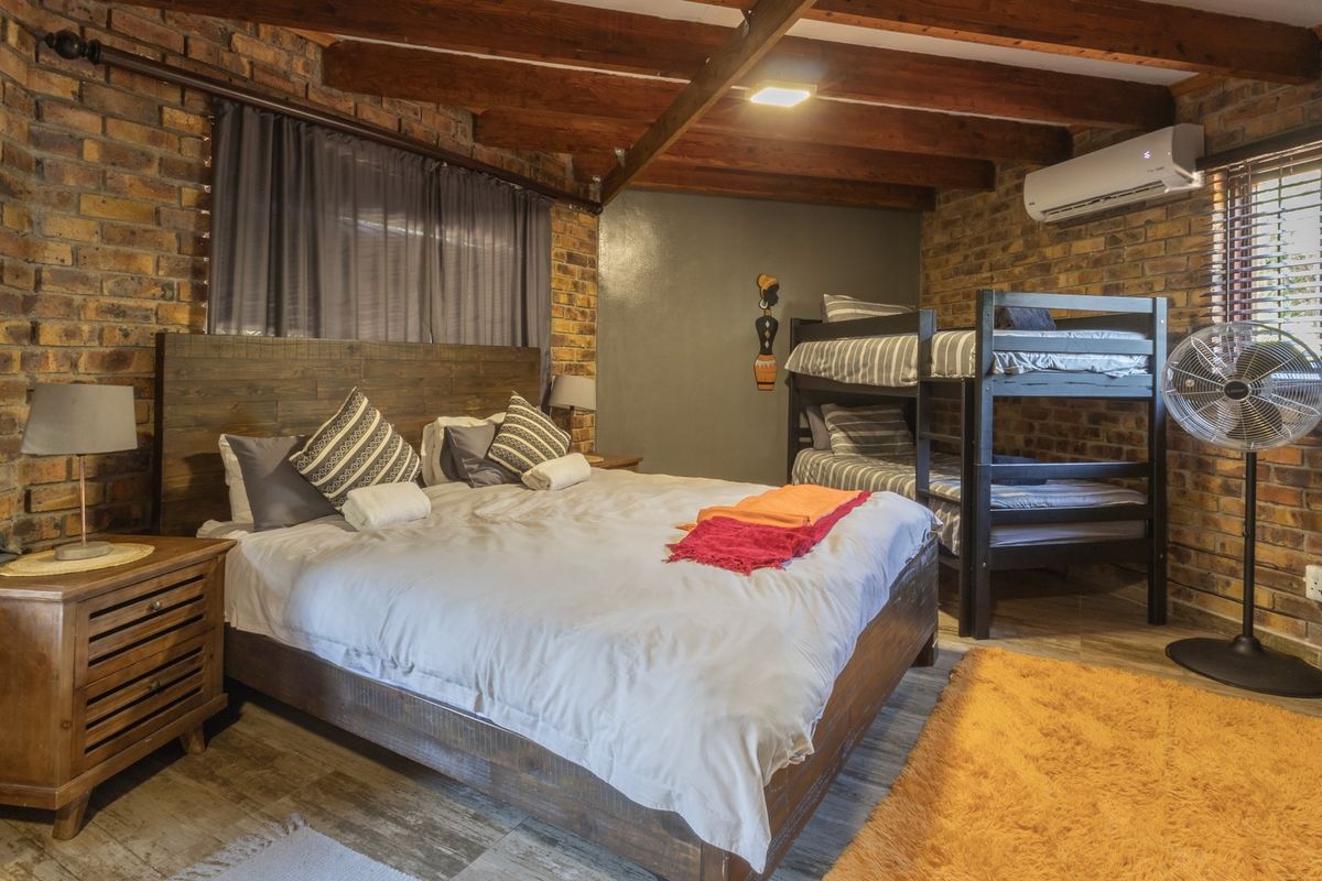 A rustic-style bedroom featuring exposed brick walls, timber ceiling beams, and a split-system air conditioner.