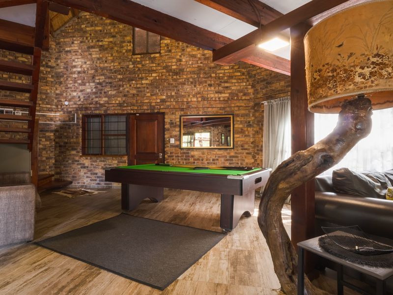 Spacious living area featuring rustic exposed brick walls, high vaulted ceilings with timber beams, and a wooden staircase.