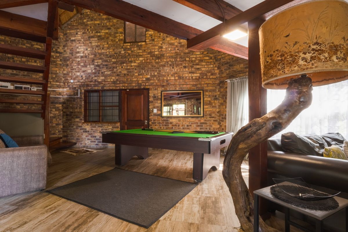 Spacious living area featuring rustic exposed brick walls, high vaulted ceilings with timber beams, and a wooden staircase.