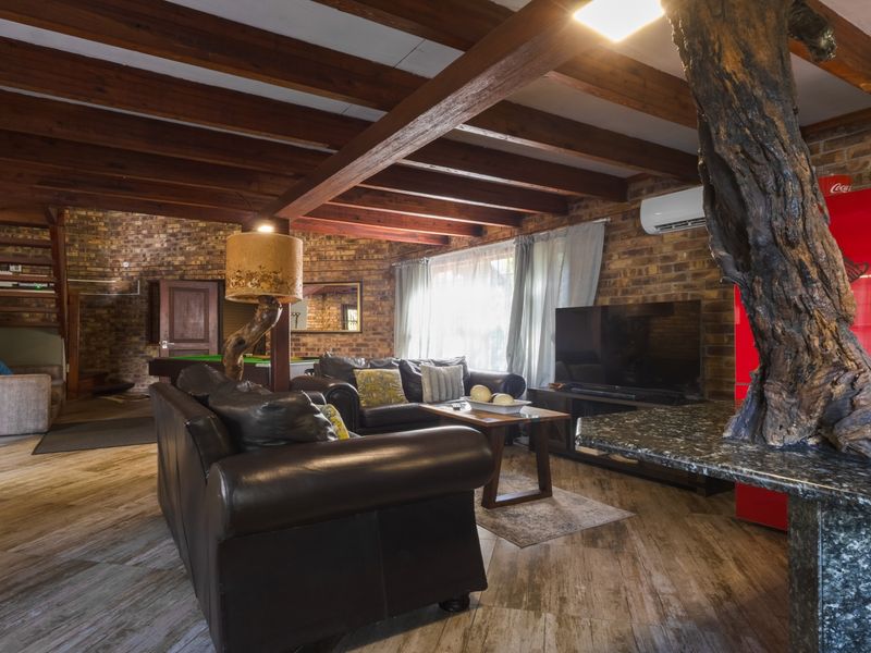 Spacious open-plan living area featuring exposed timber ceiling beams, rustic facebrick walls, and a unique granite breakfast bar with integrated natural wood element.