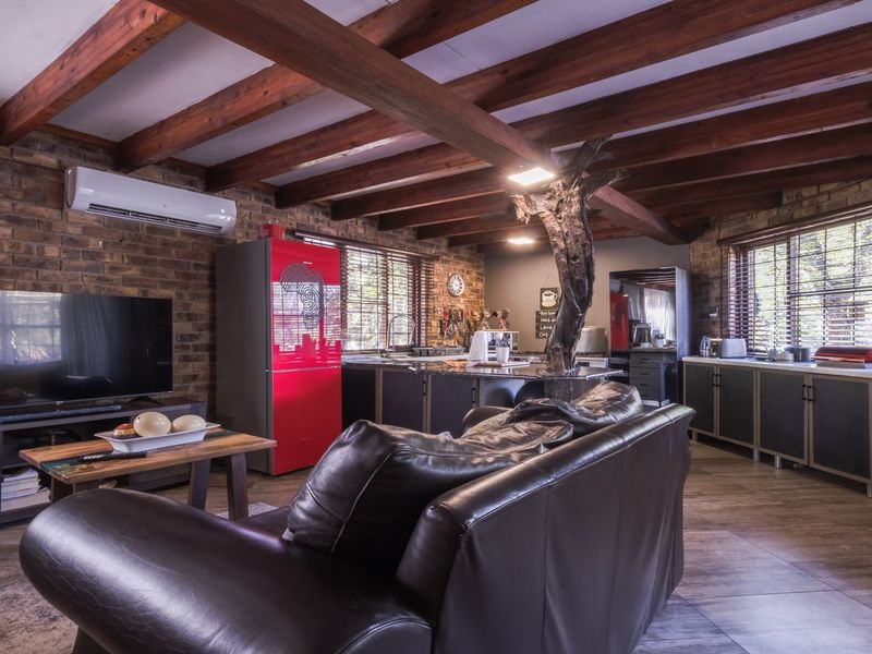 Spacious open-plan living and kitchen area featuring exposed timber beams, rustic brick walls, modern cabinetry, and tiled flooring throughout.