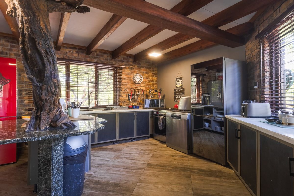 Rustic kitchen featuring exposed brick walls, timber ceiling beams, granite countertops, and ample built-in cabinetry with a unique integrated tree feature.