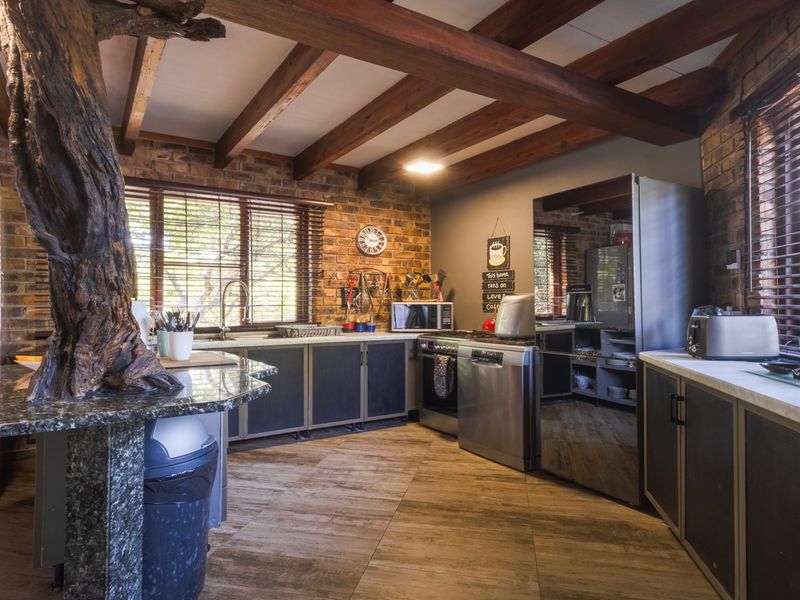 Rustic kitchen featuring exposed brick walls, timber ceiling beams, granite countertops, and ample built-in cabinetry with a unique integrated tree feature.