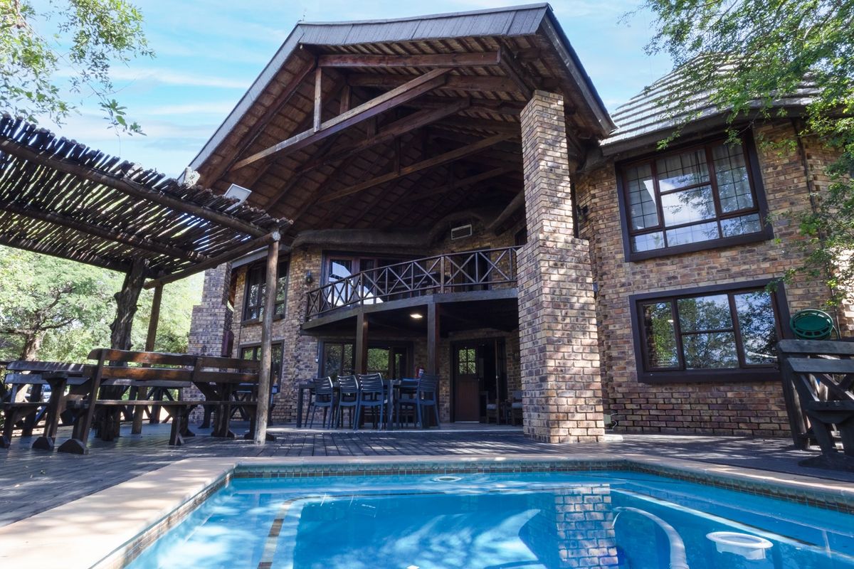 Rear exterior view featuring a swimming pool, timber decking, a covered patio area, and a multi-level brick house with a thatched roof.