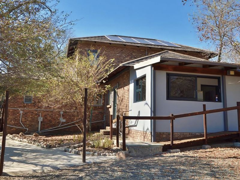 Rear view of the property featuring a brick facade, solar panels on the roof, and a timber access ramp leading to the entrance.