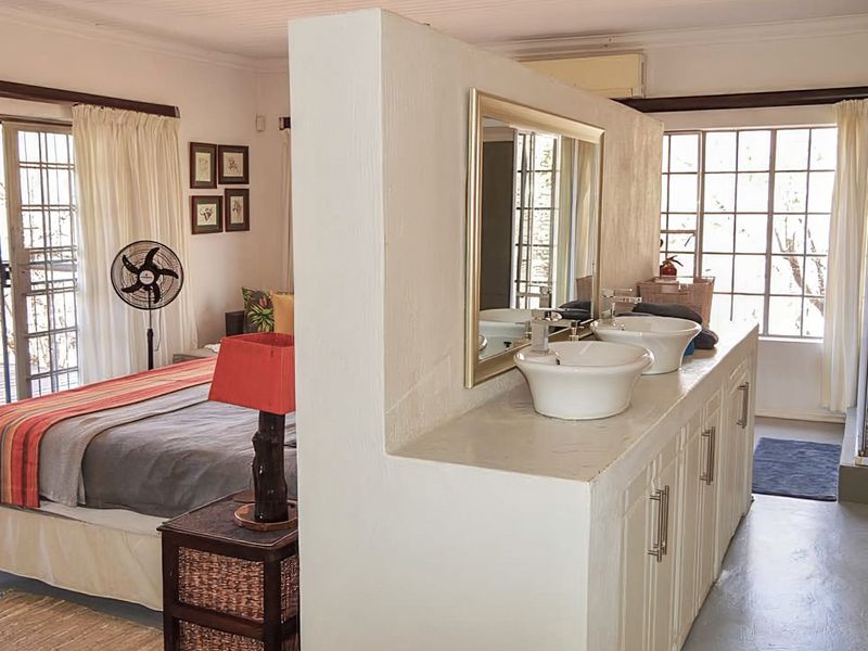 Open-plan bedroom featuring an integrated en-suite bathroom with a double vanity, vessel sinks, and a separate shower enclosure, with direct access to a patio.