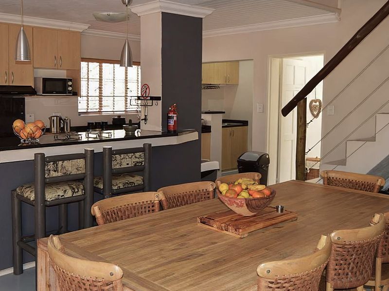 Open-plan kitchen and dining area featuring built-in cabinetry, granite countertops, a breakfast bar, and a staircase leading to the upper level.