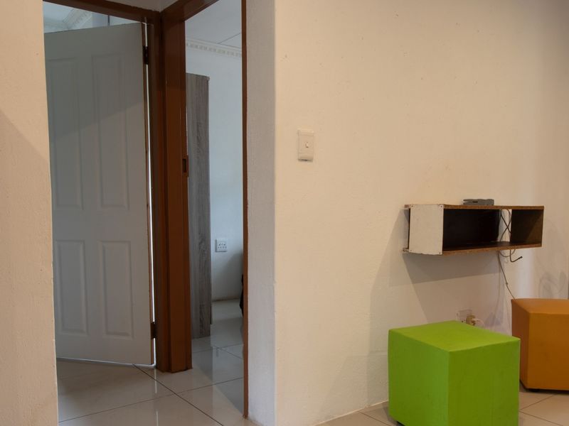 A view of a living area showing tiled flooring, internal doors, and wall-mounted shelving with visible electrical wiring.
