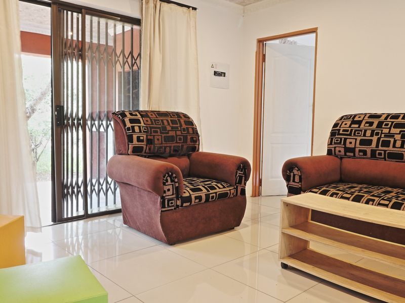 A living room featuring light-colored floor tiles, a sliding glass door with a security gate, and access to an adjacent room.