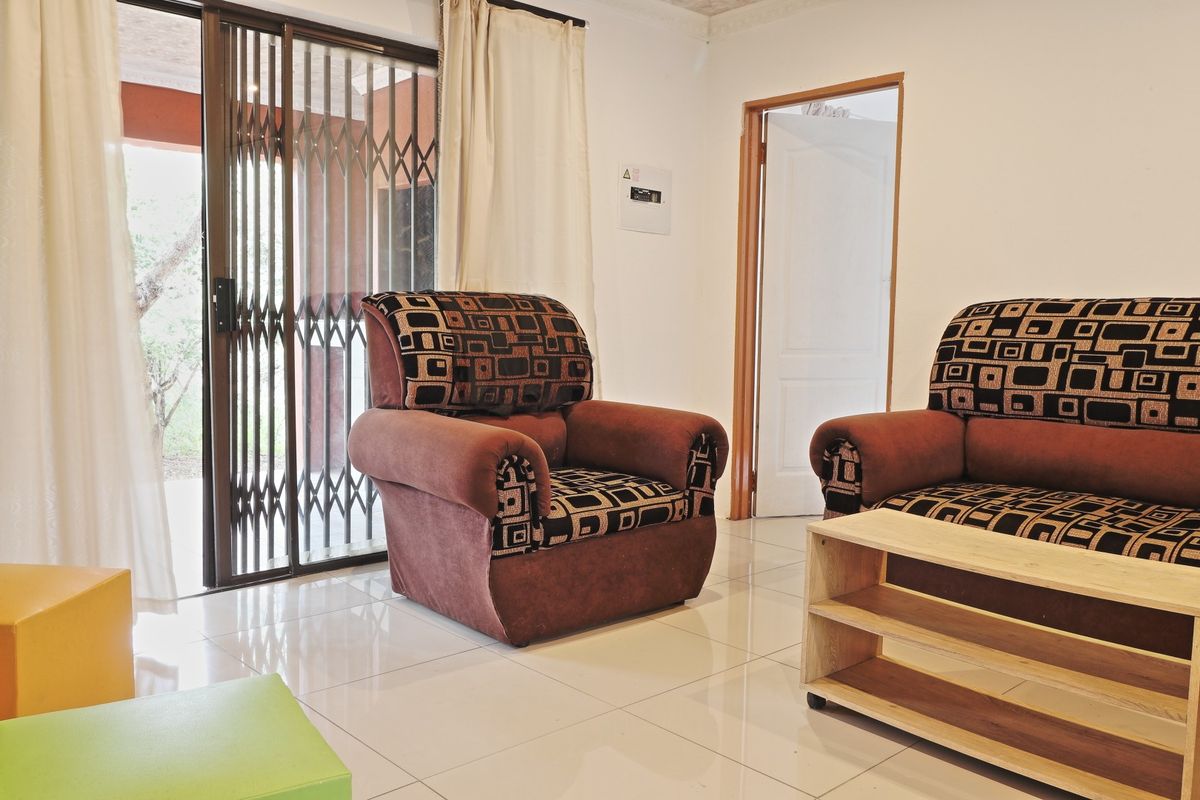 A living room featuring light-colored floor tiles, a sliding glass door with a security gate, and access to an adjacent room.