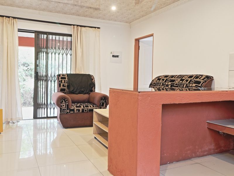 Open plan living area featuring tiled flooring, a built-in breakfast bar, and a sliding glass door with security gate leading to the exterior.