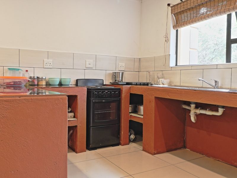 A functional kitchen featuring built-in masonry cabinetry, a freestanding stove, tiled backsplash, and a stainless steel sink with exposed plumbing.