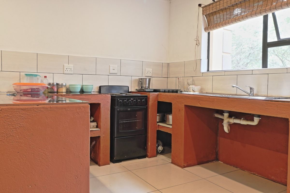 A functional kitchen featuring built-in masonry cabinetry, a freestanding stove, tiled backsplash, and a stainless steel sink with exposed plumbing.