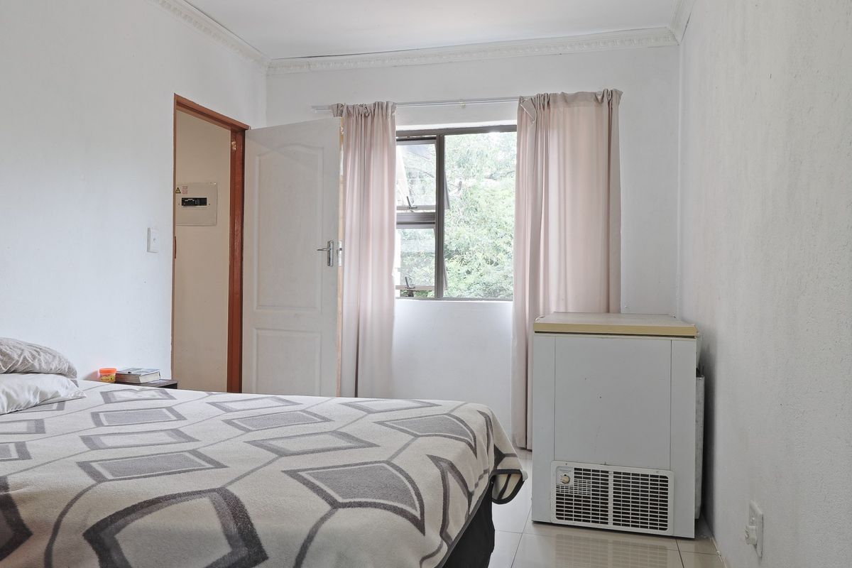 A bedroom featuring tiled flooring, crown molding, and a window with natural light. The space includes a built-in electrical distribution board.