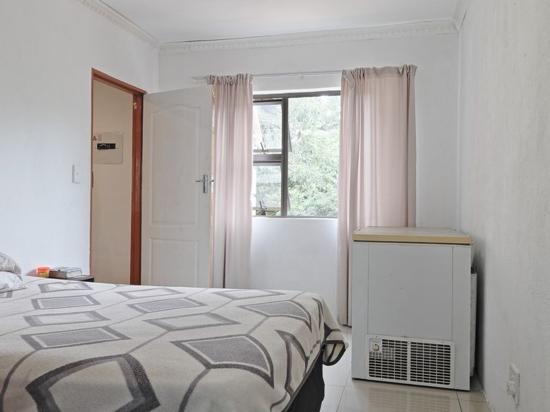 A bedroom featuring tiled flooring, crown molding, and a window with natural light. The space includes a built-in electrical distribution board.