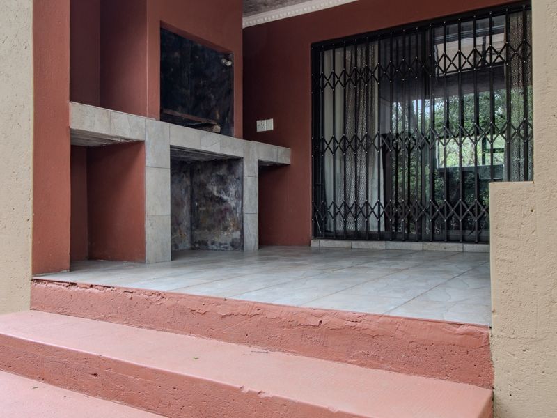 Covered patio area featuring a built-in braai, tiled flooring, and a secure sliding door entrance.
