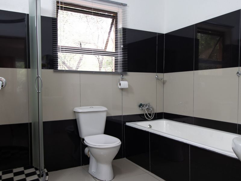 A modern bathroom featuring a bathtub, separate shower enclosure, toilet, and basin with high-contrast black and beige wall tiling.