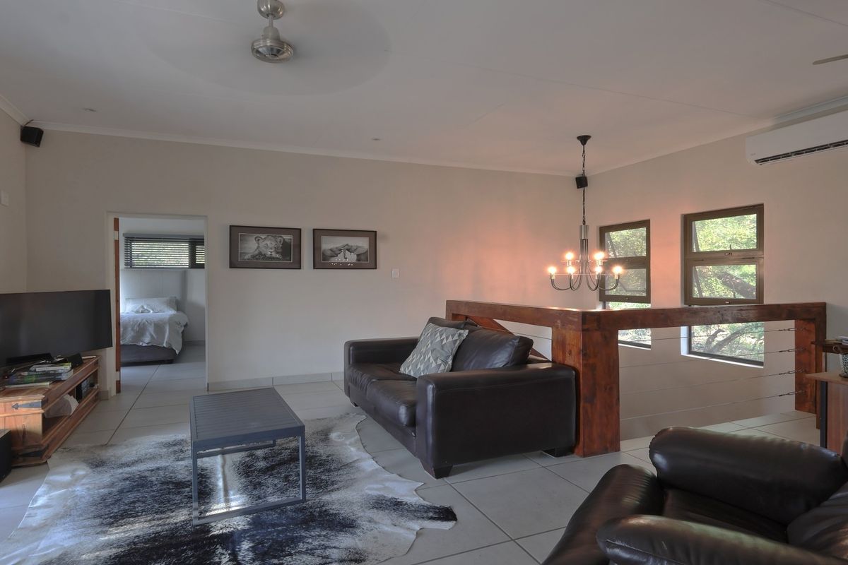 Spacious living area featuring tiled flooring, a timber balustrade, ceiling fan, and a wall-mounted split-system air conditioner, with an adjacent bedroom visible.