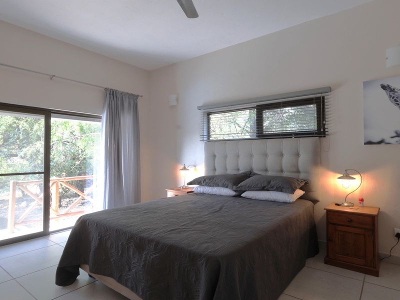 A well-lit bedroom featuring tiled flooring, a ceiling fan, and a large sliding glass door providing access to an outdoor area.