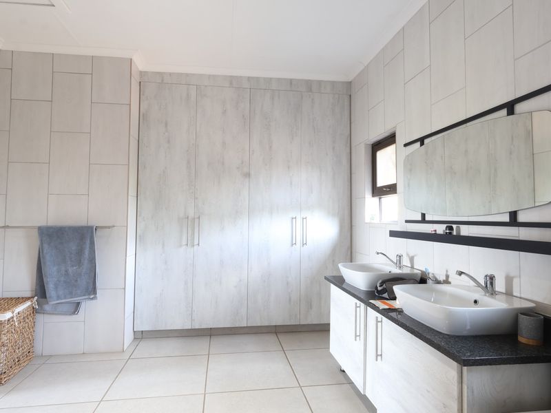 Modern bathroom featuring a double vanity with vessel sinks, extensive built-in cabinetry, and neutral floor-to-ceiling wall tiling.