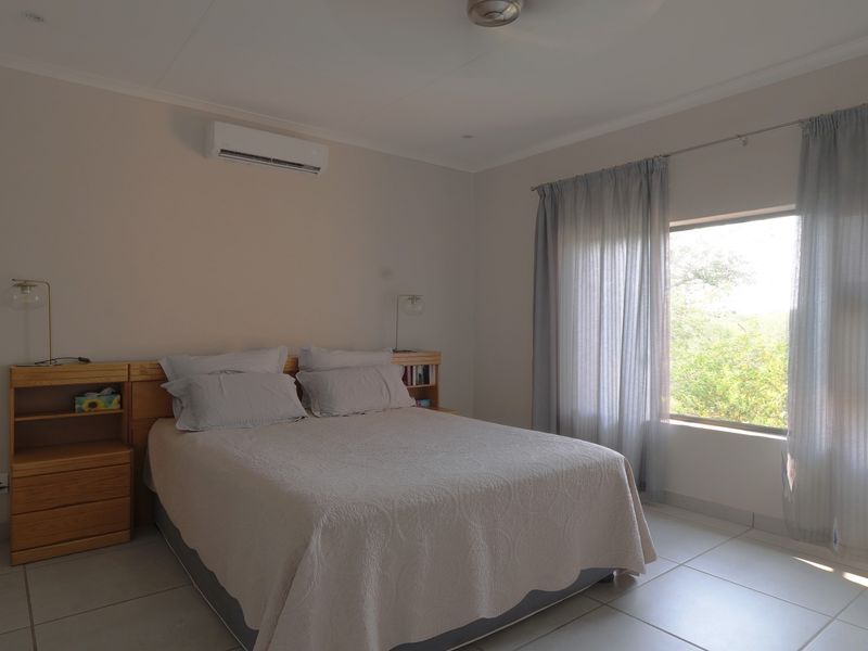 A well-maintained bedroom featuring tiled flooring, a built-in headboard with integrated shelving, and a wall-mounted split-system air conditioner.