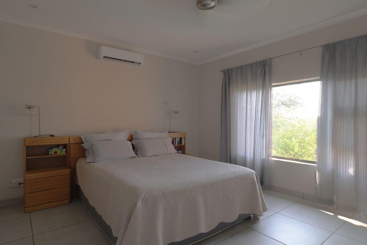 A well-maintained bedroom featuring tiled flooring, a built-in headboard with integrated shelving, and a wall-mounted split-system air conditioner.