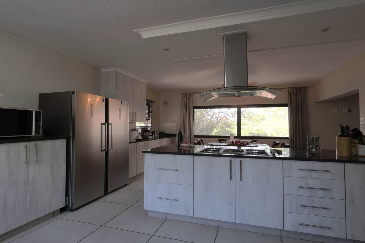 Modern kitchen featuring a central island with a gas hob, stainless steel extractor fan, ample built-in cabinetry, and stone countertops.