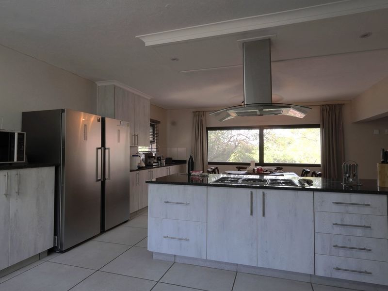 Modern kitchen featuring a central island with a gas hob, stainless steel extractor fan, ample built-in cabinetry, and stone countertops.