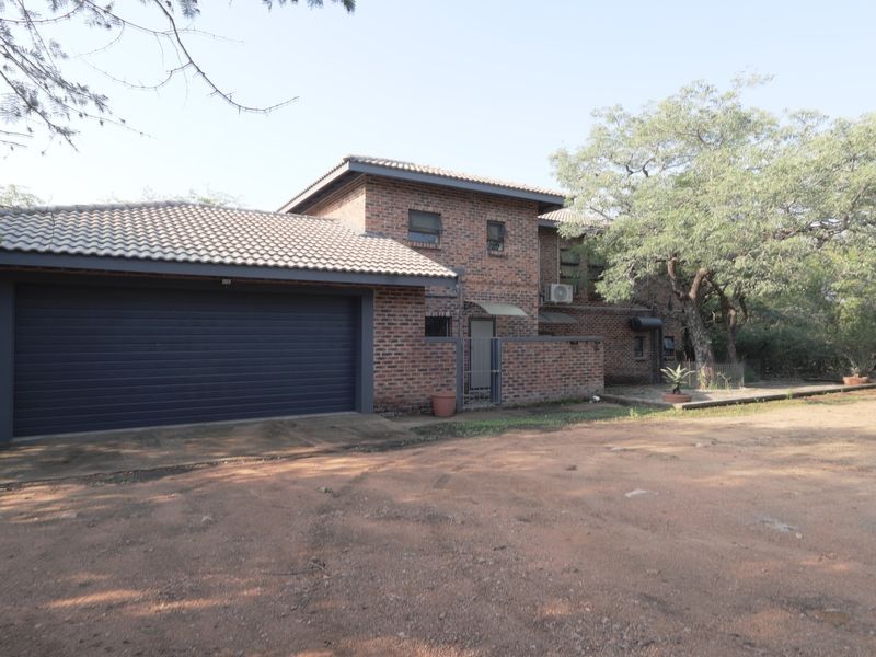 Front view of a double-story face brick house featuring a double garage, tiled roof, and an unpaved driveway area.