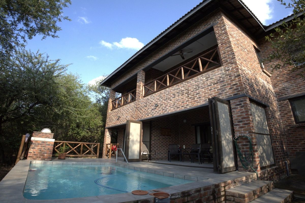 Rear view of a double-story exposed brick house featuring a swimming pool, ground-floor patio, and an upper-level balcony with timber railings.