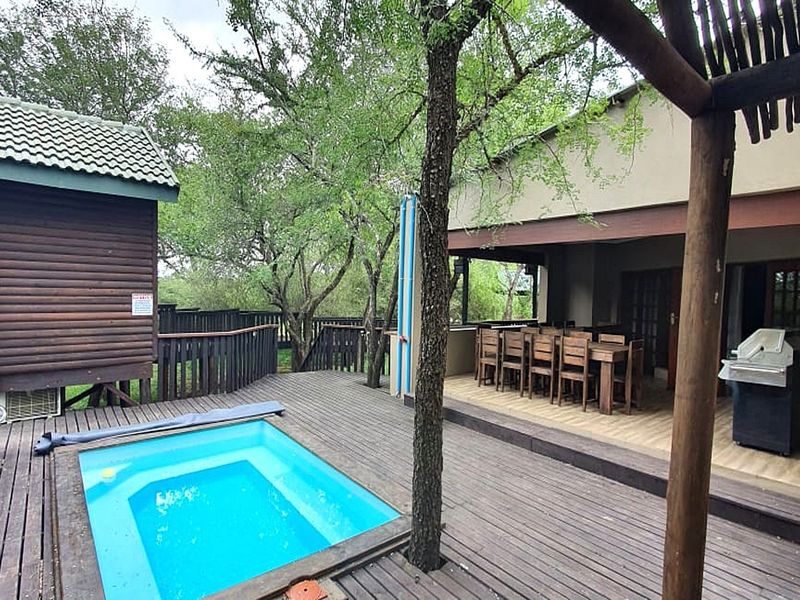Outdoor entertainment area featuring a swimming pool, timber decking, and a covered patio space adjacent to a log cabin structure.