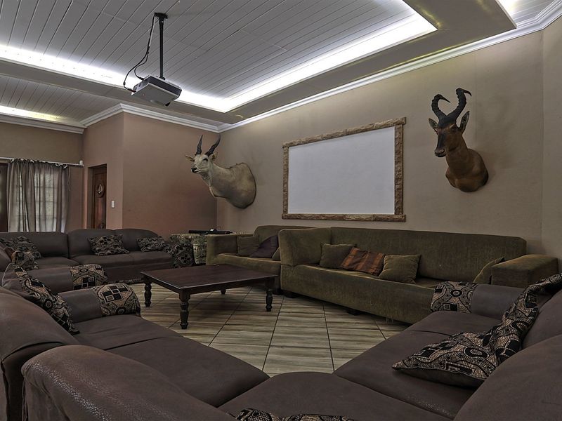 A dedicated cinema room featuring a ceiling-mounted projector, projection screen, recessed cove lighting, and tiled flooring with access to the outdoors via french doors.