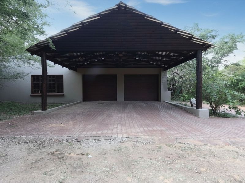 A double garage featuring a timber-framed roof structure and a paved driveway, set within a natural, wooded environment.