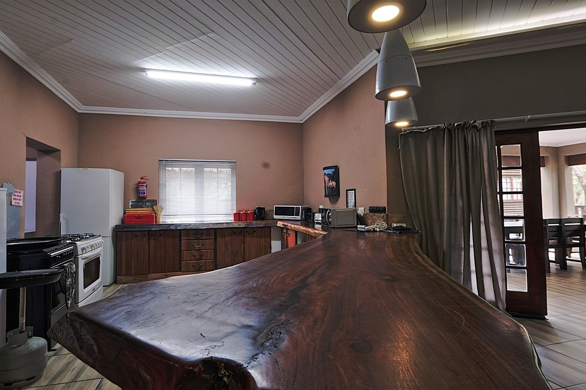 A rustic kitchen featuring a large natural wood slab breakfast bar, wooden cabinetry, and tiled flooring, with direct access to an outdoor patio area.