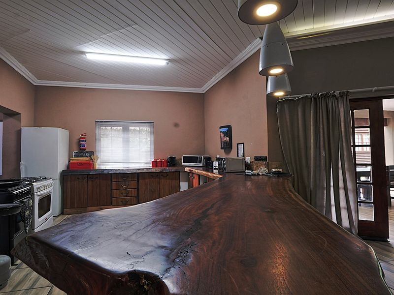 A rustic kitchen featuring a large natural wood slab breakfast bar, wooden cabinetry, and tiled flooring, with direct access to an outdoor patio area.