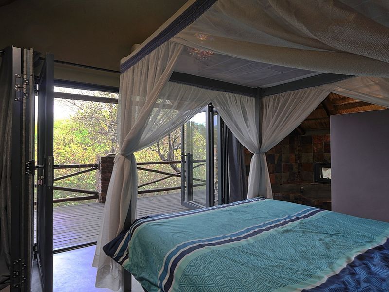 Spacious bedroom featuring a thatched roof, stone accent wall, and bi-fold doors opening onto a private wooden deck with natural views.