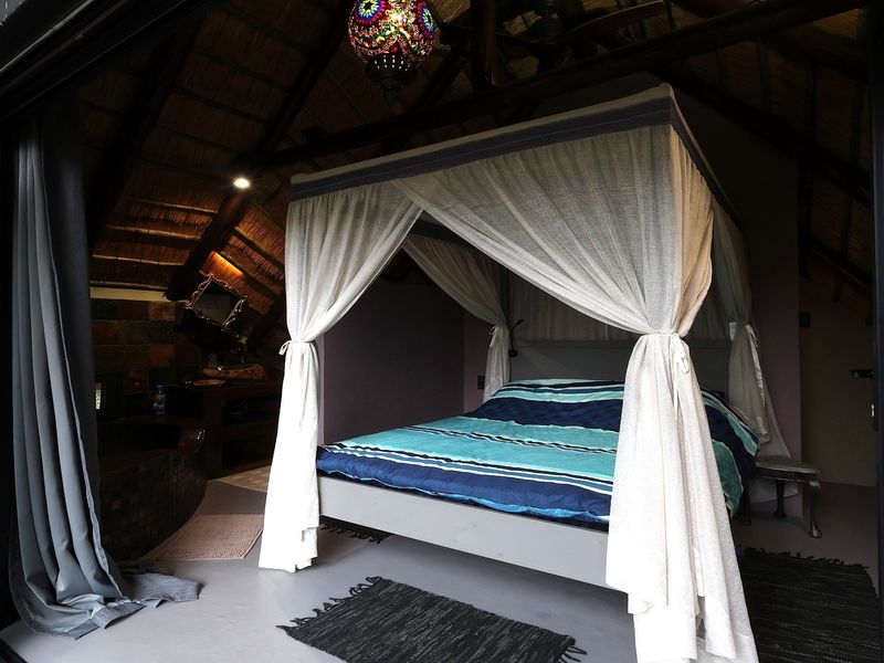 A unique bedroom featuring a high vaulted ceiling with exposed timber rafters, thatched roofing, and large sliding glass doors opening to the exterior.
