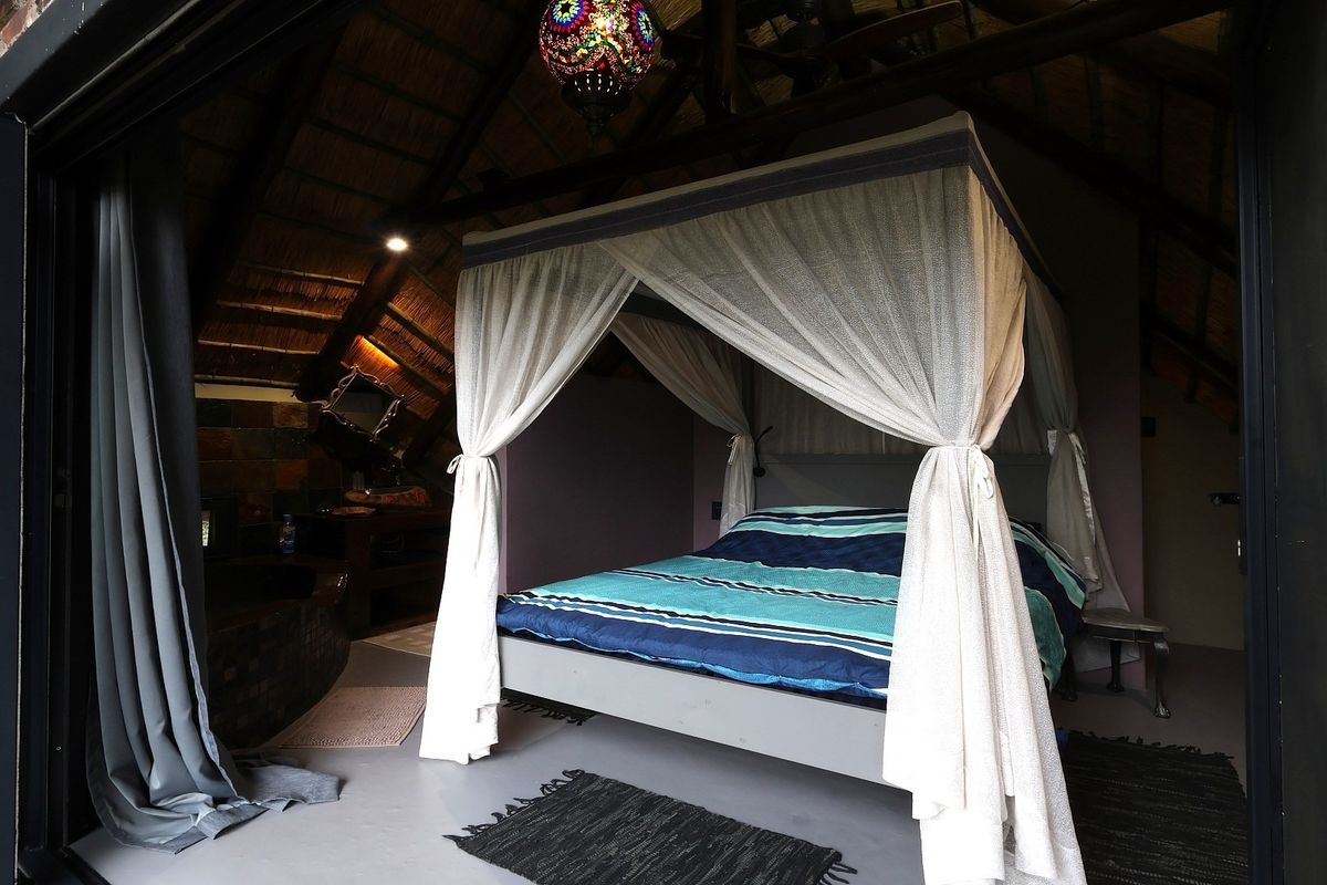A unique bedroom featuring a high vaulted ceiling with exposed timber rafters, thatched roofing, and large sliding glass doors opening to the exterior.