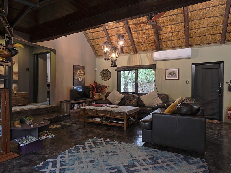 Spacious living room featuring a high exposed timber and thatched ceiling, polished concrete floors, a spiral staircase, and integrated solar power infrastructure.